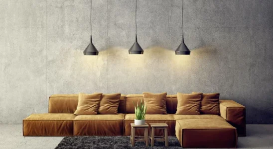 Concreto na decoração da parede com sofá marrom em ele e tapete marrom pelo alto retangular com dois banquinhos de madeira com planta em vaso branco.