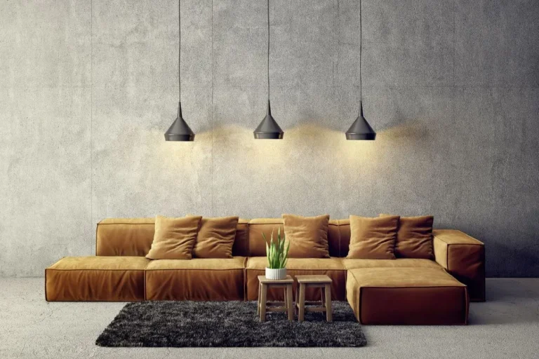 Concreto na decoração da parede com sofá marrom em ele e tapete marrom pelo alto retangular com dois banquinhos de madeira com planta em vaso branco.